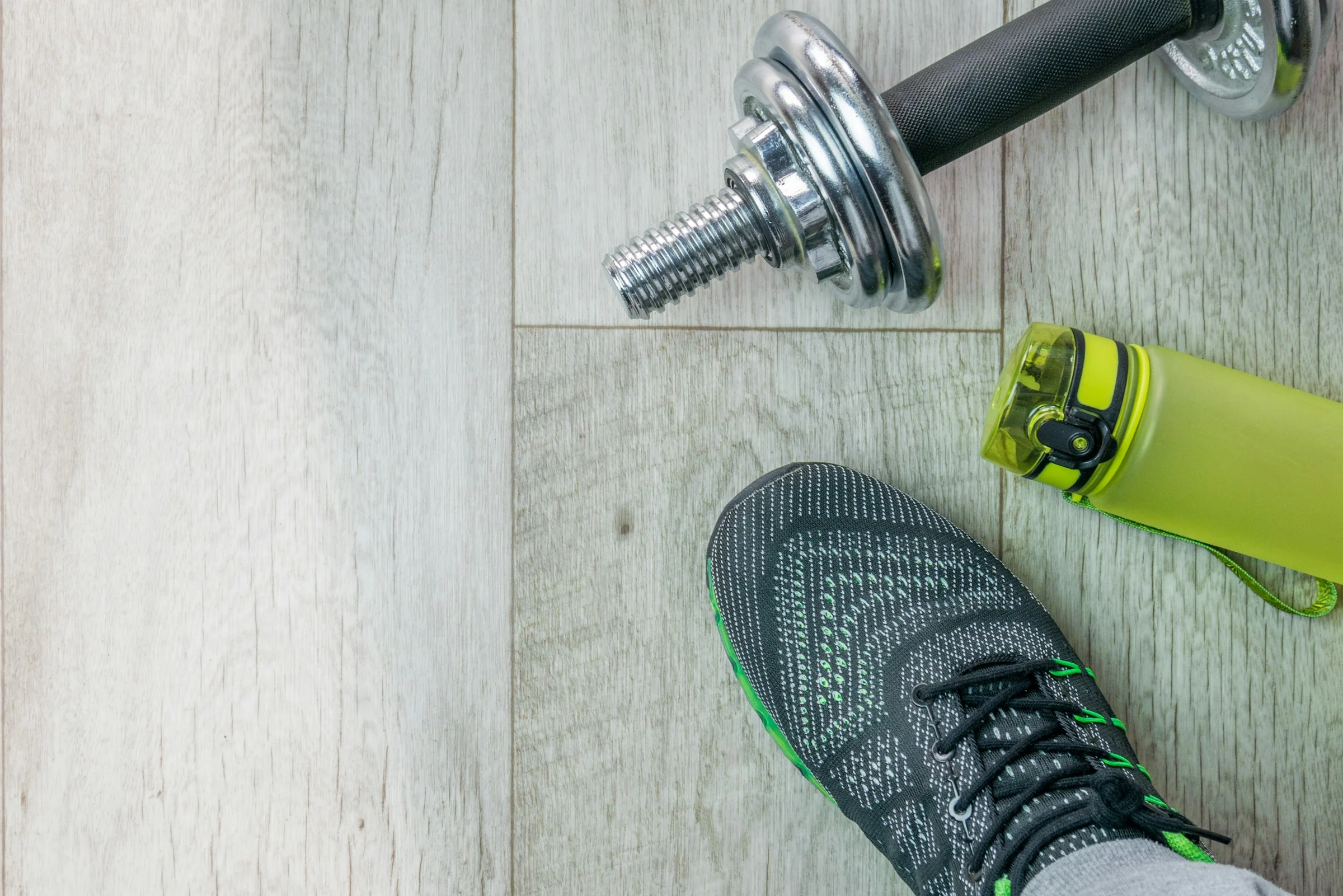 Training shoe, water bottle and dumbbell prepared on a wooden floor